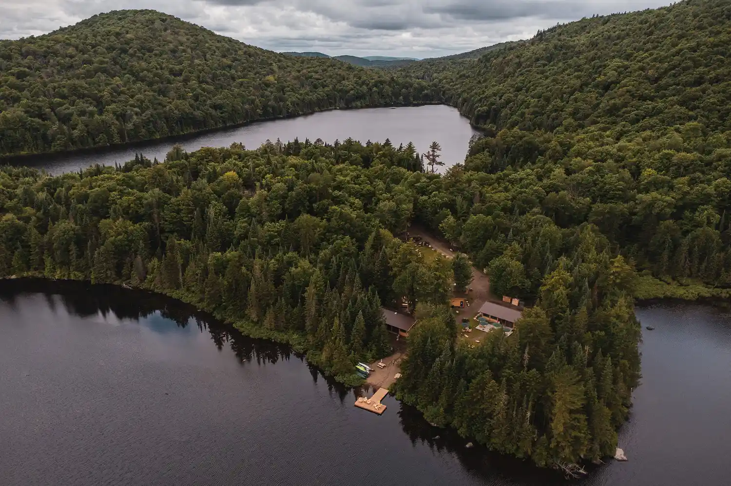 High-angle drone shot of the Huttopia Les Deux Lacs resort showing the lakefront and forest canopy.