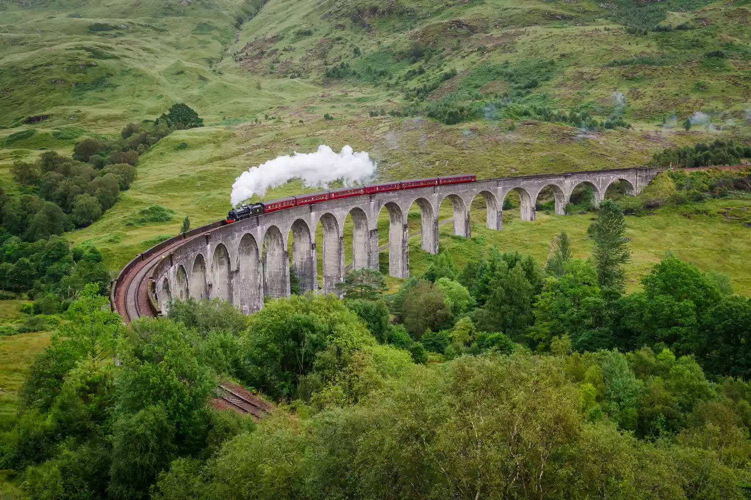 The Jacobite steam train crossing the curved stone arches of the Glenfinnan Viaduct.