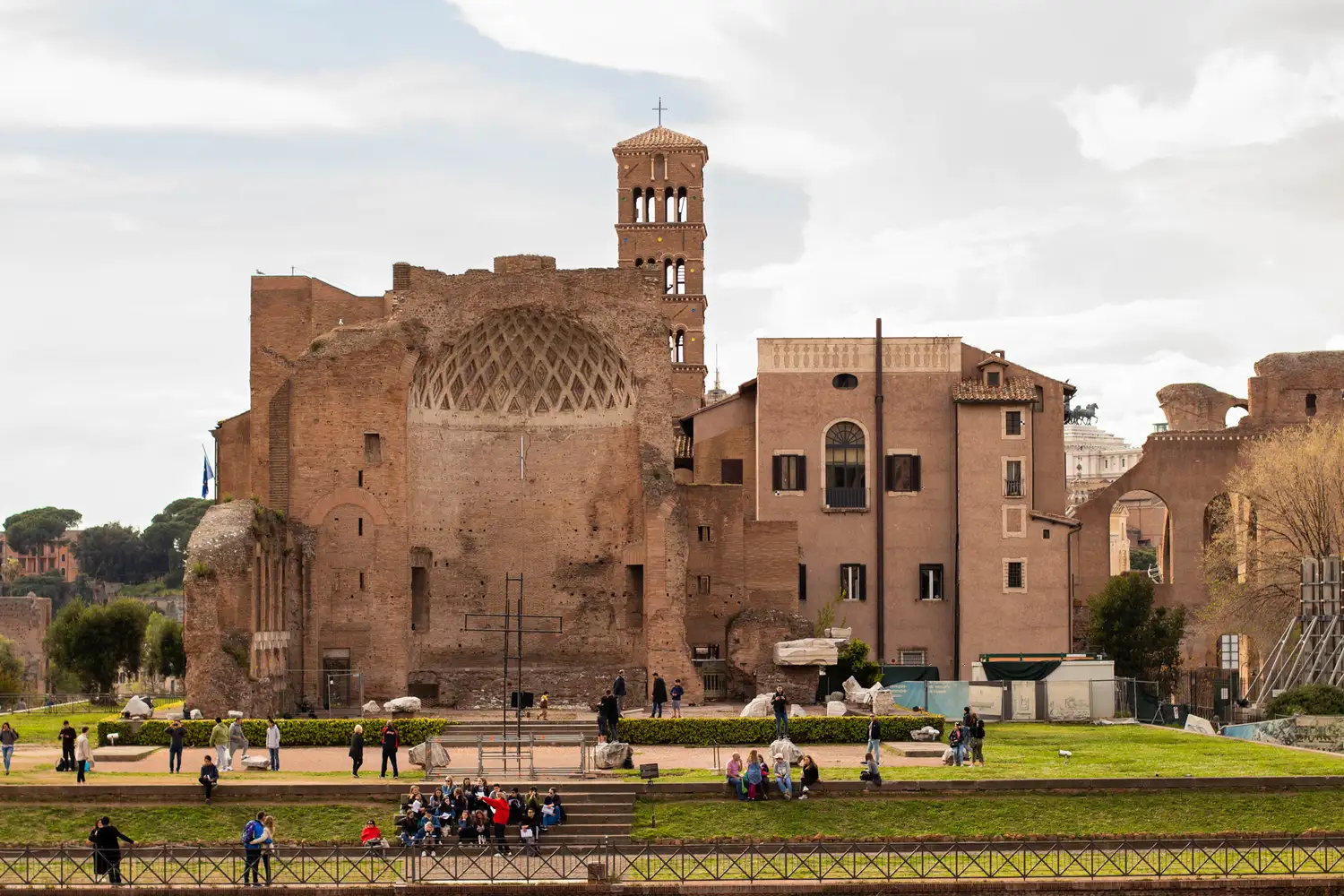 An ancient architectural site in Rome with a group of people gathered near the base.