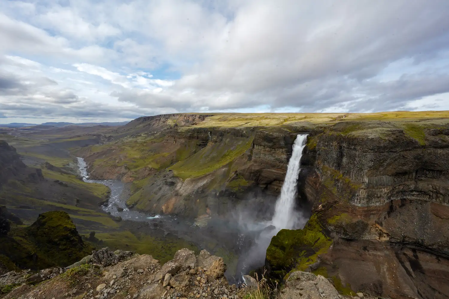 A powerful waterfall plunging into a deep canyon surrounded by rugged, rocky cliffs.