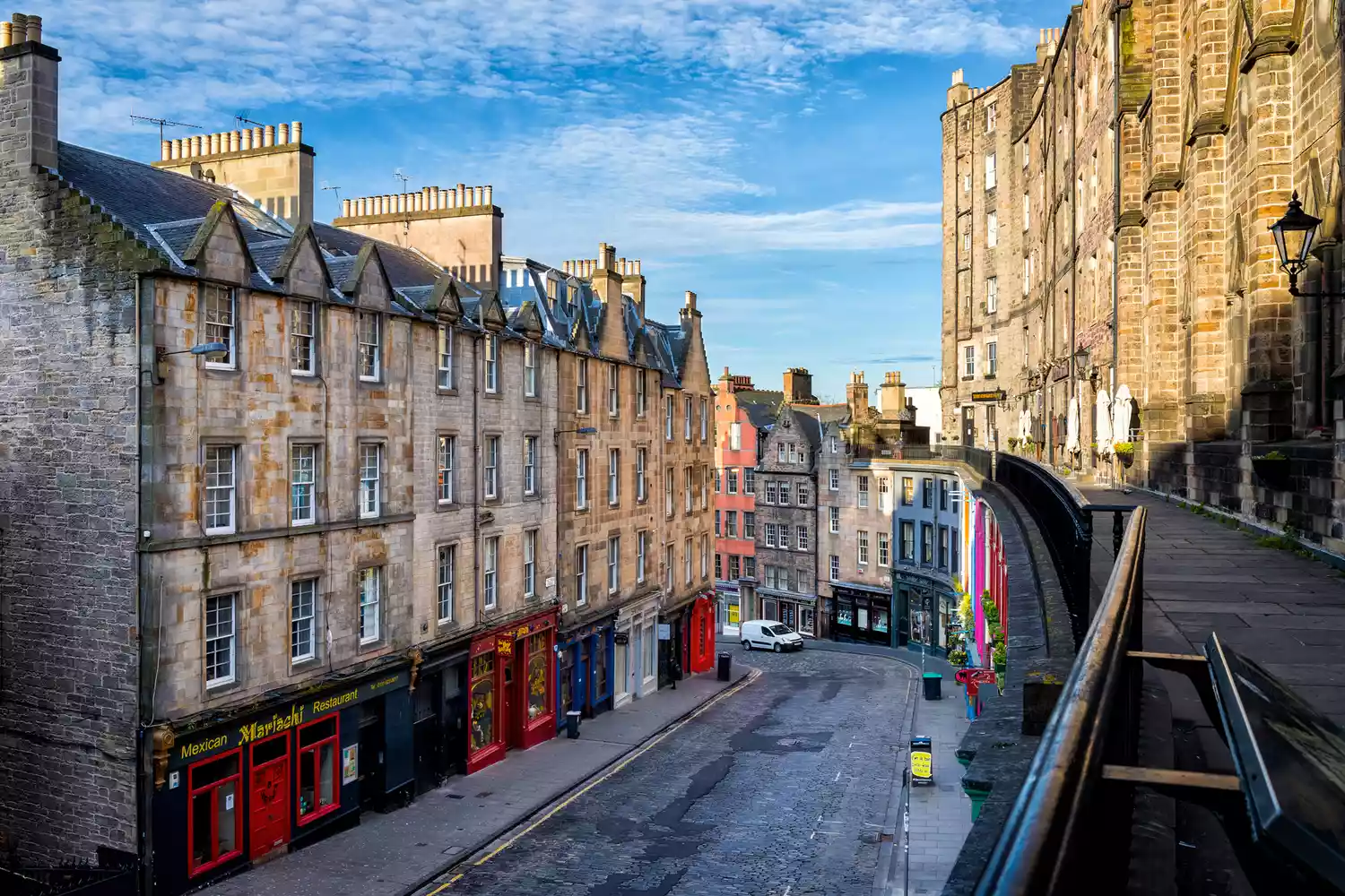 A colorful curved street with historic stone buildings in Edinburgh's Old Town.