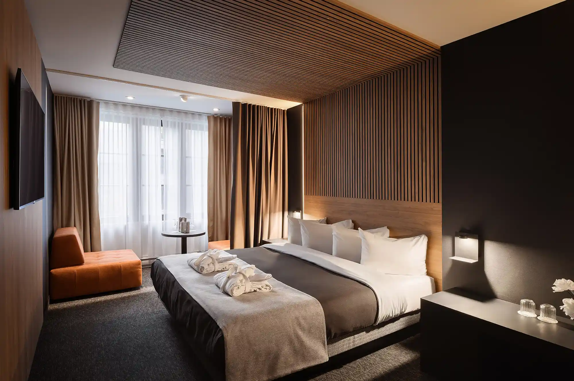 Minimalist hotel room with warm wood paneling, a large window, and clean white bedding.