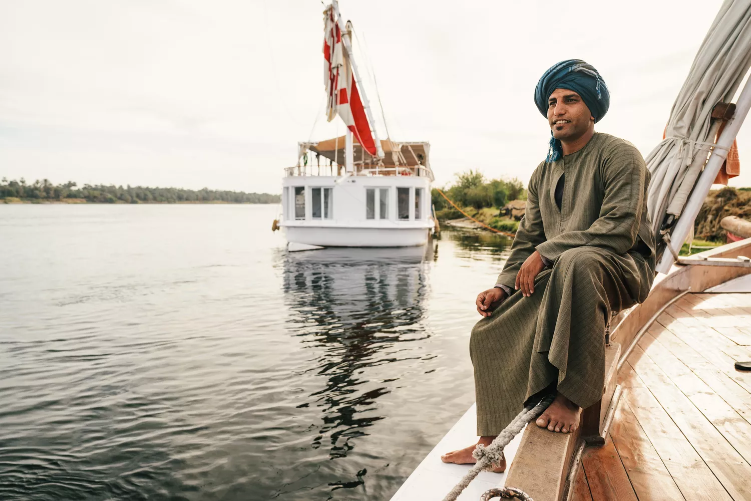 A smiling crew member in traditional attire on the deck of a dahabiya.