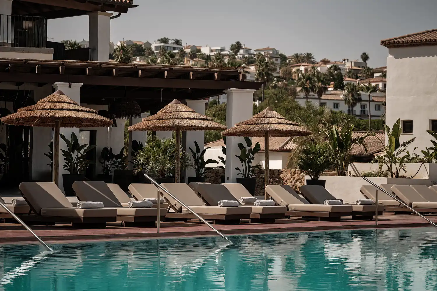 Row of sun loungers under straw umbrellas by the tiered pool at Oku Andalusia.
