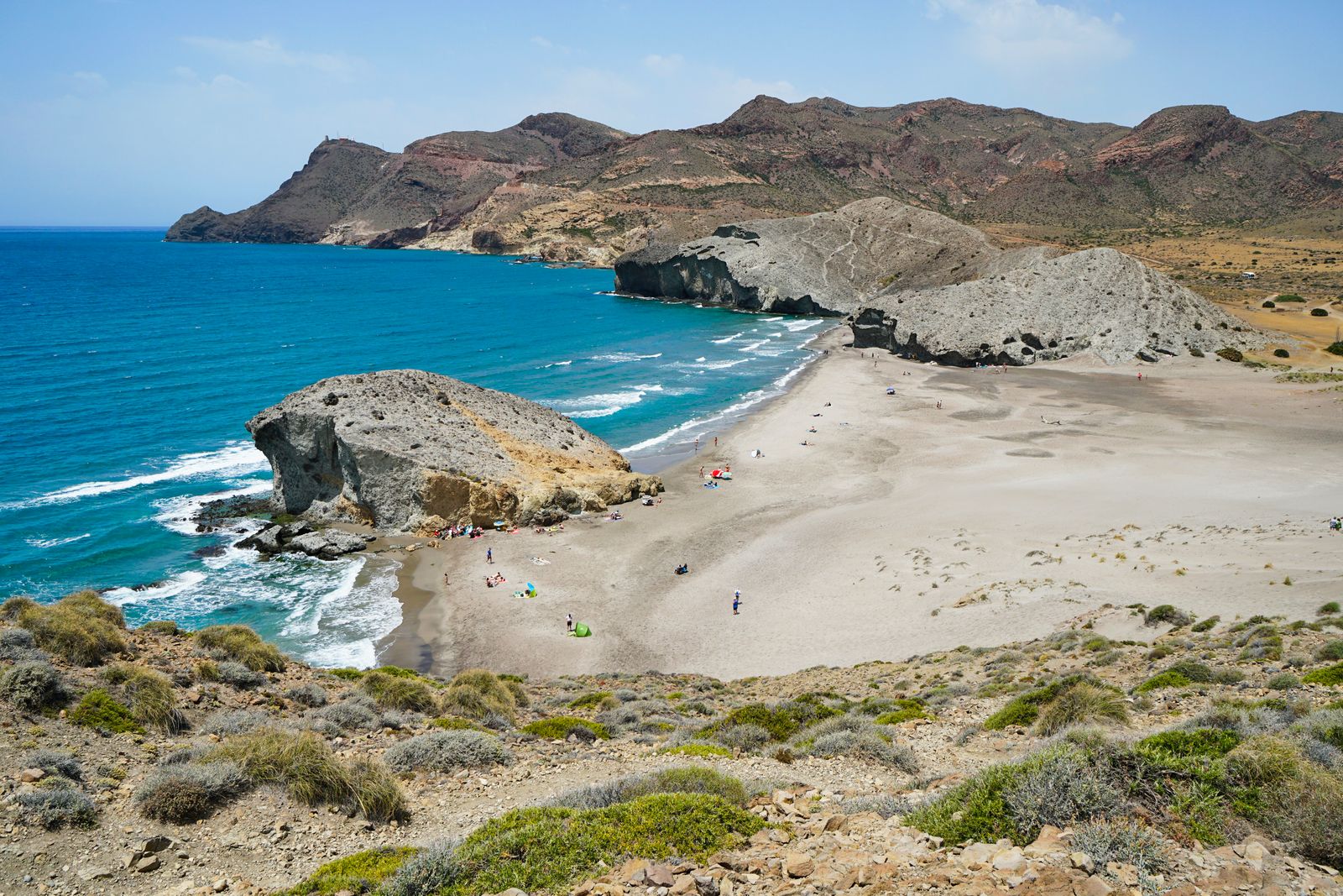 A motorcycle parked on a high cliff overlooking a rugged beach and volcanic rock formations.