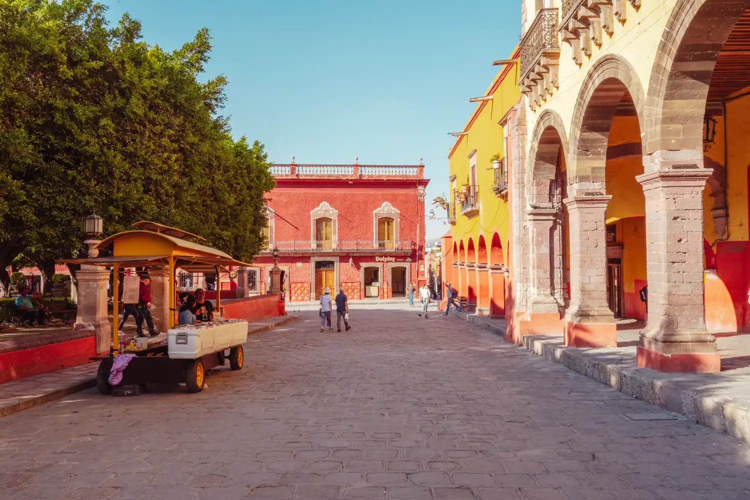 A street scene in San Miguel de Allende with colorful colonial buildings and people walking.