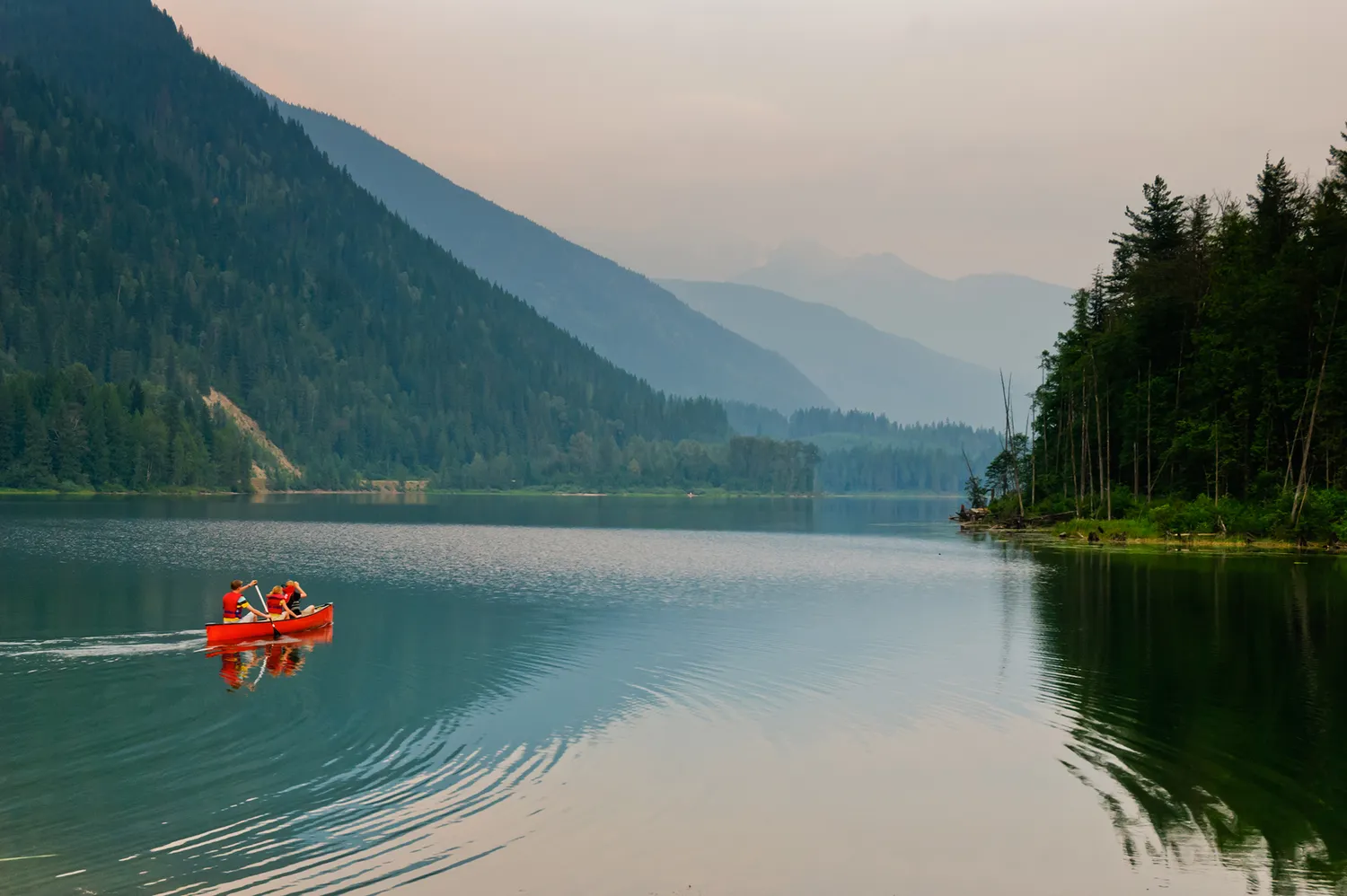 Canoers paddling on the calm, reflective surface of an alpine lake surrounded by mountains.