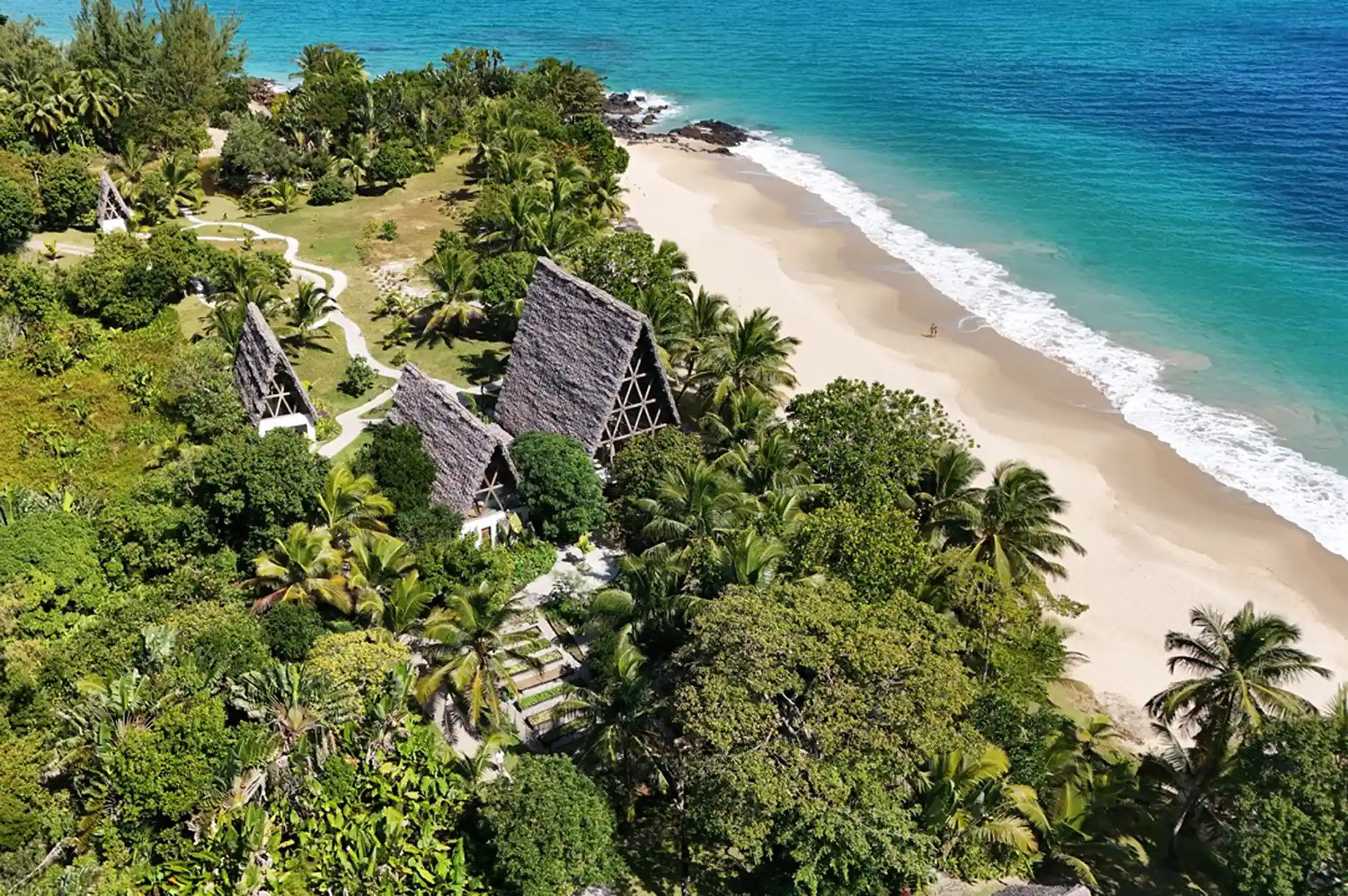 A tropical beachfront with huts and palm trees under a clear blue sky.