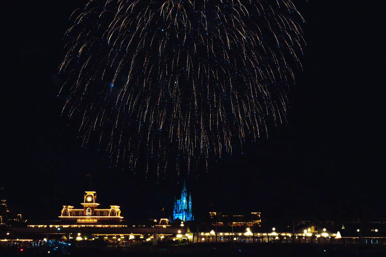 Colorful fireworks exploding over the Disney skyline as seen from a boat on the water.