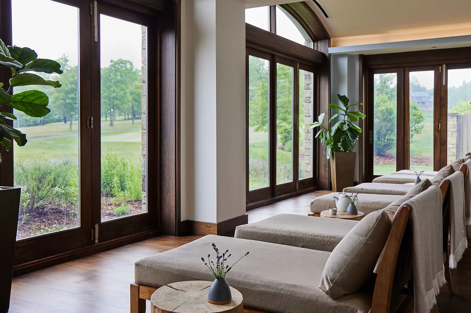 Relaxation room with lounge chairs and large windows looking out at green trees.