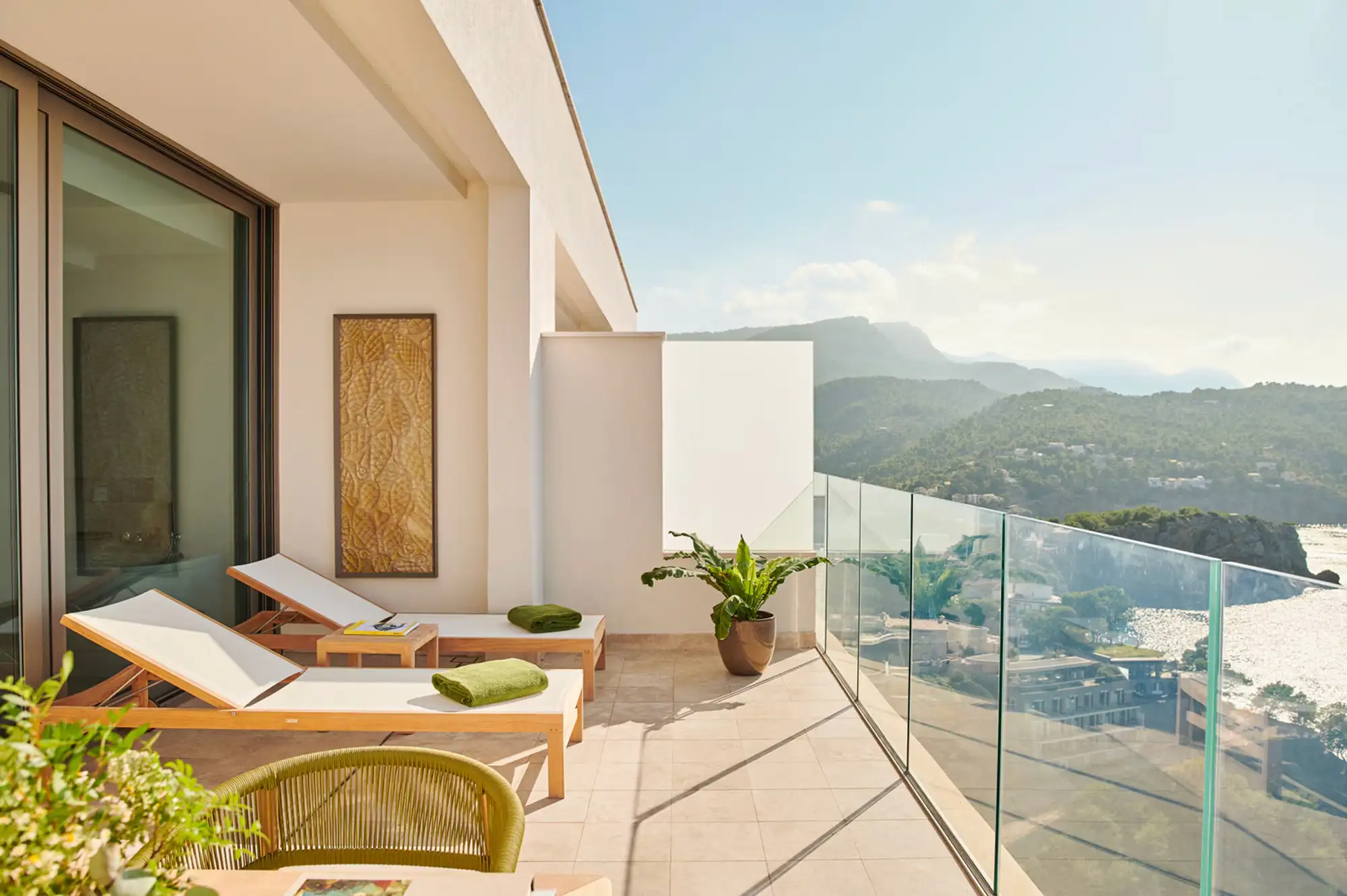 A luxury terrace with lounge chairs overlooking a mountain valley and the ocean.