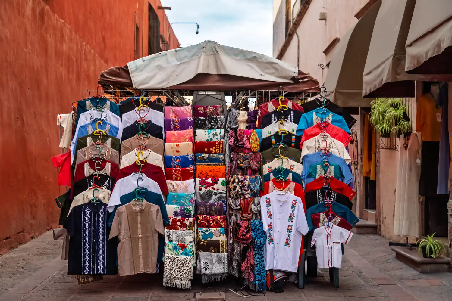 A colorful street market stall in Querétaro filled with traditional Mexican textiles and handcrafted clothes.