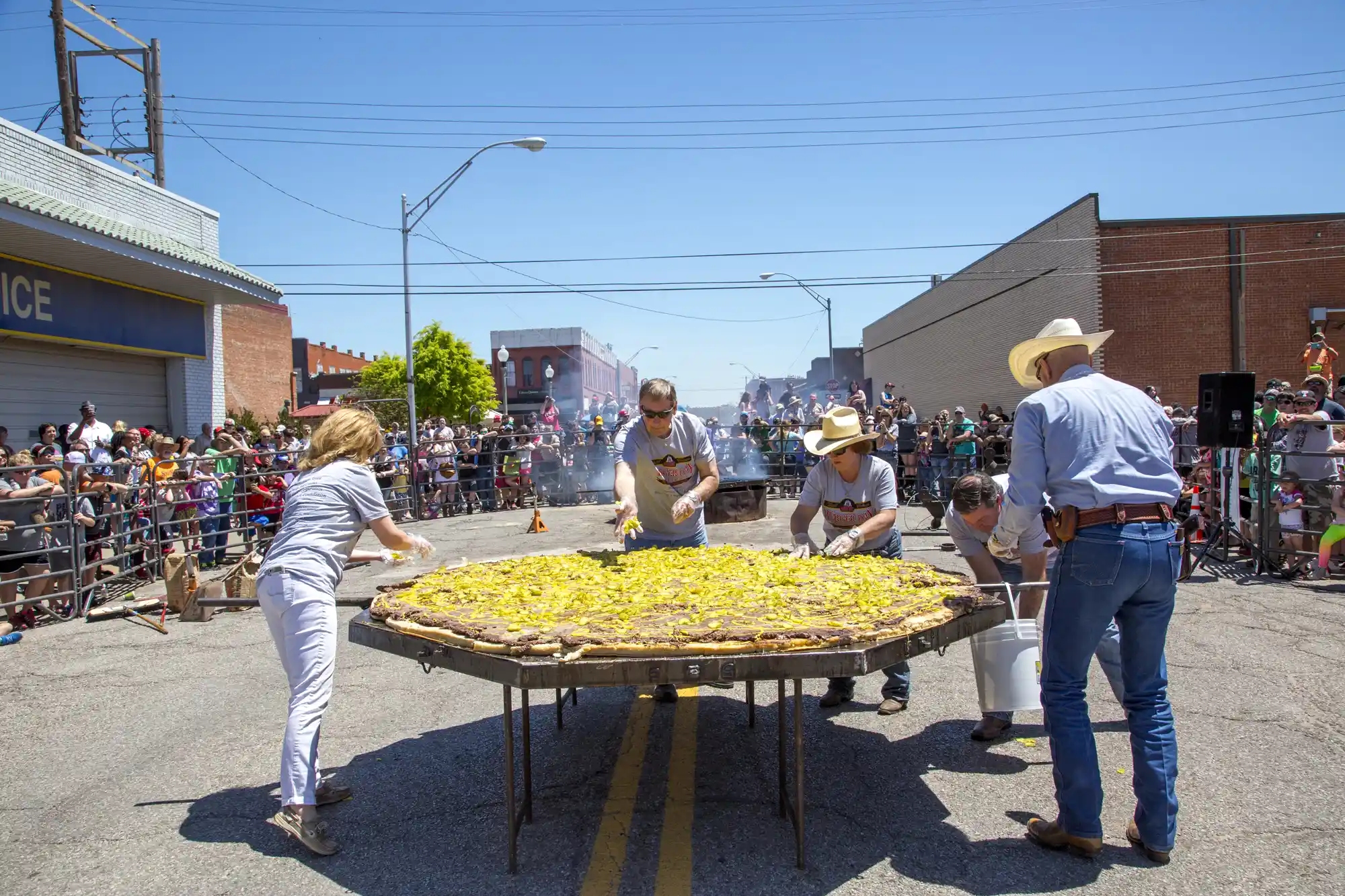 A large crowd gathered around a giant griddle outdoors during a public food festival.