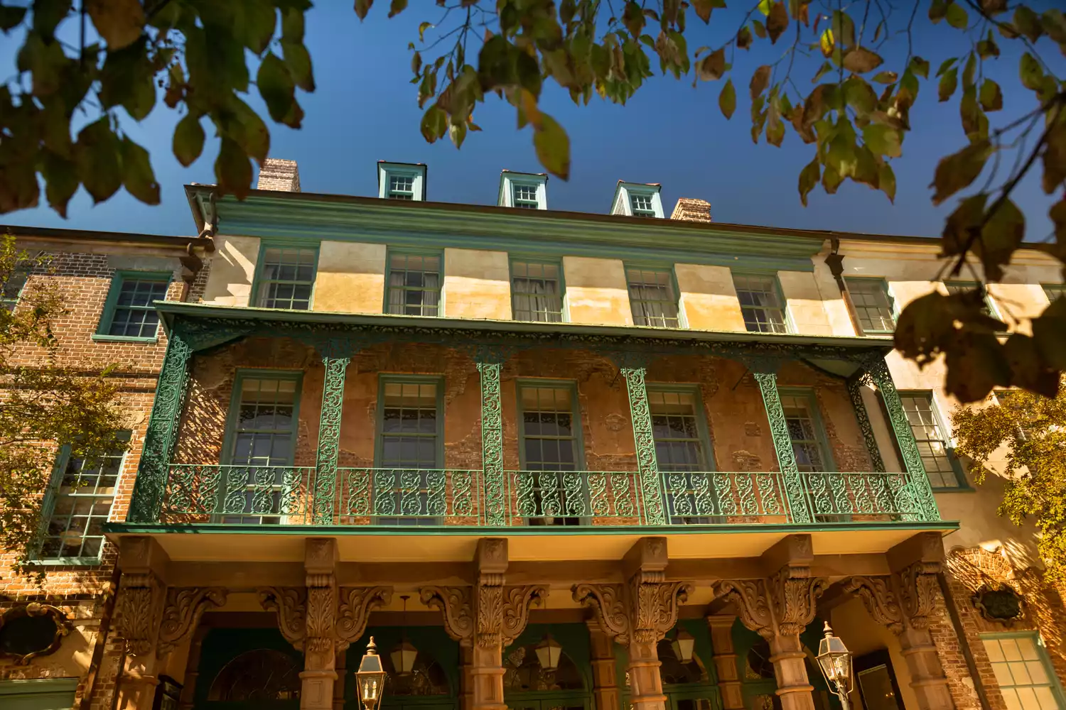 Ornate green balconies of the historic Dock Street Theatre against a sunny yellow facade.