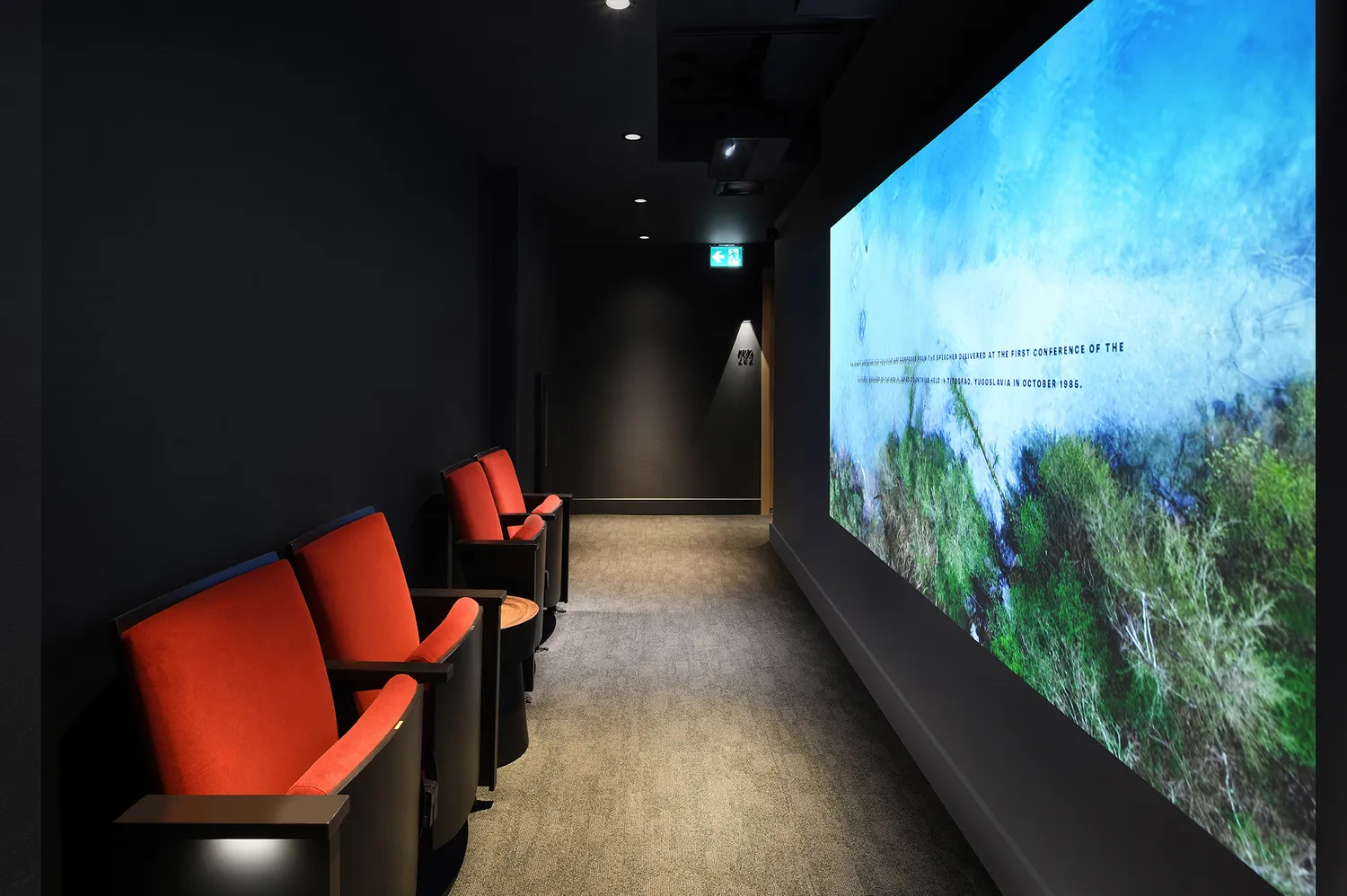 A hotel hallway with red armchairs and a wall-sized projection of a forest scene.