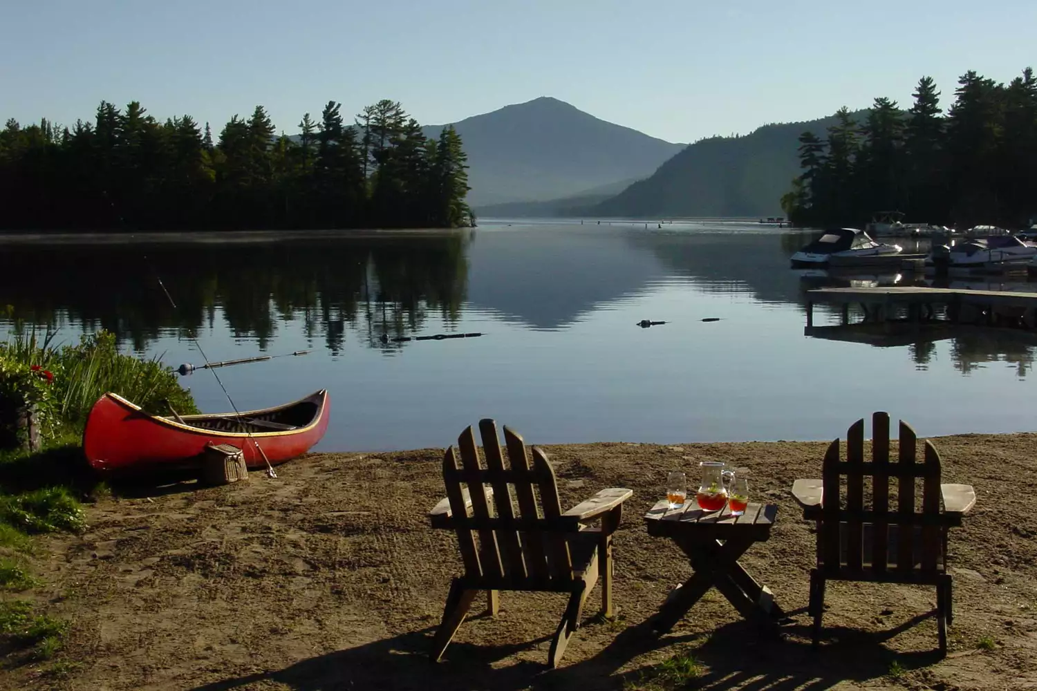 Canoes and Adirondack chairs situated on a dock at Whiteface Lodge with mountains in the background.