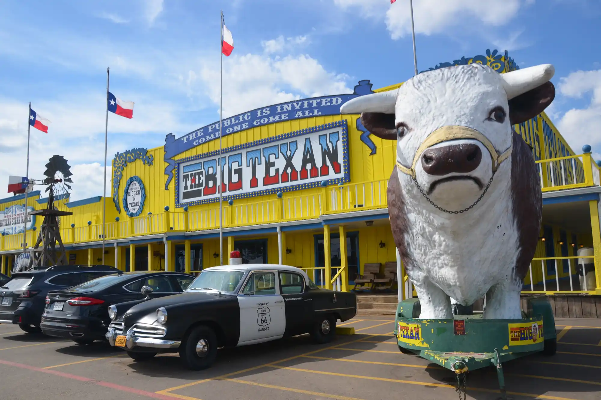 Exterior of The Big Texan Steak Ranch in Amarillo featuring its famous giant cow statue and a vintage police car.