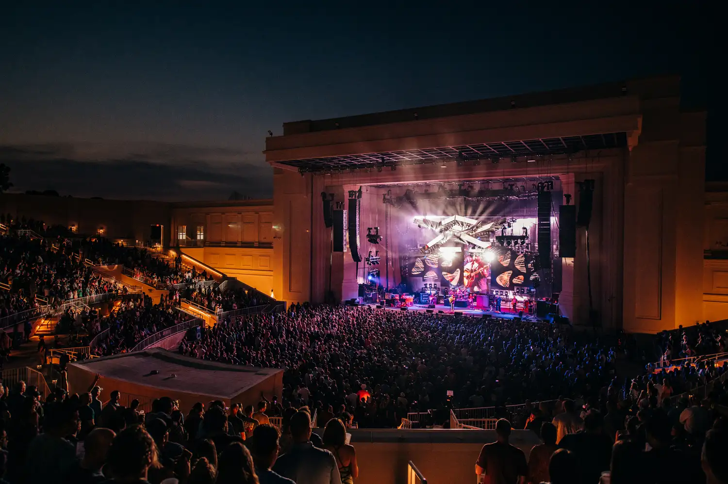 A live concert at the Orion Amphitheater with purple stage lighting and a large crowd.