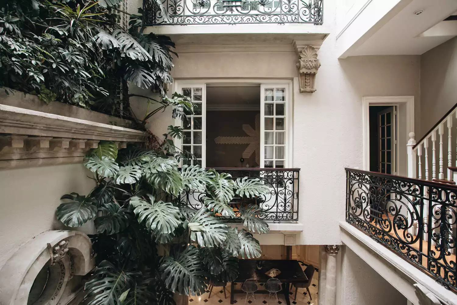The verdant inner courtyard of Nima Local House with lush greenery and neoclassical architectural details.