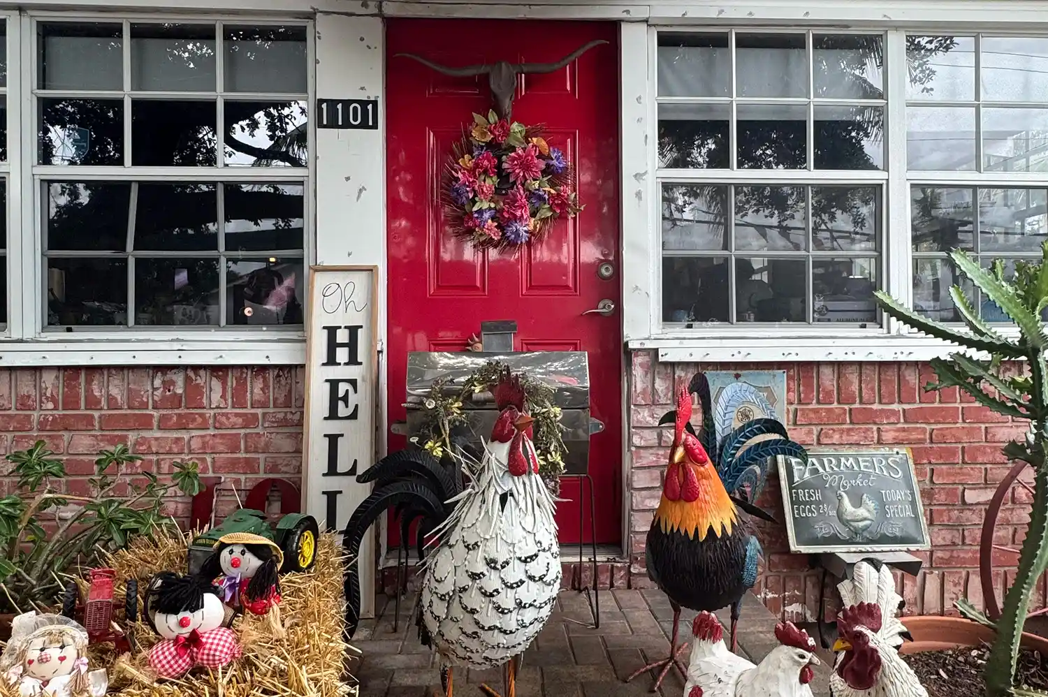 A decorated entryway with a red door, a wreath, rooster figurines, and seasonal decorations at Regina's Farm.