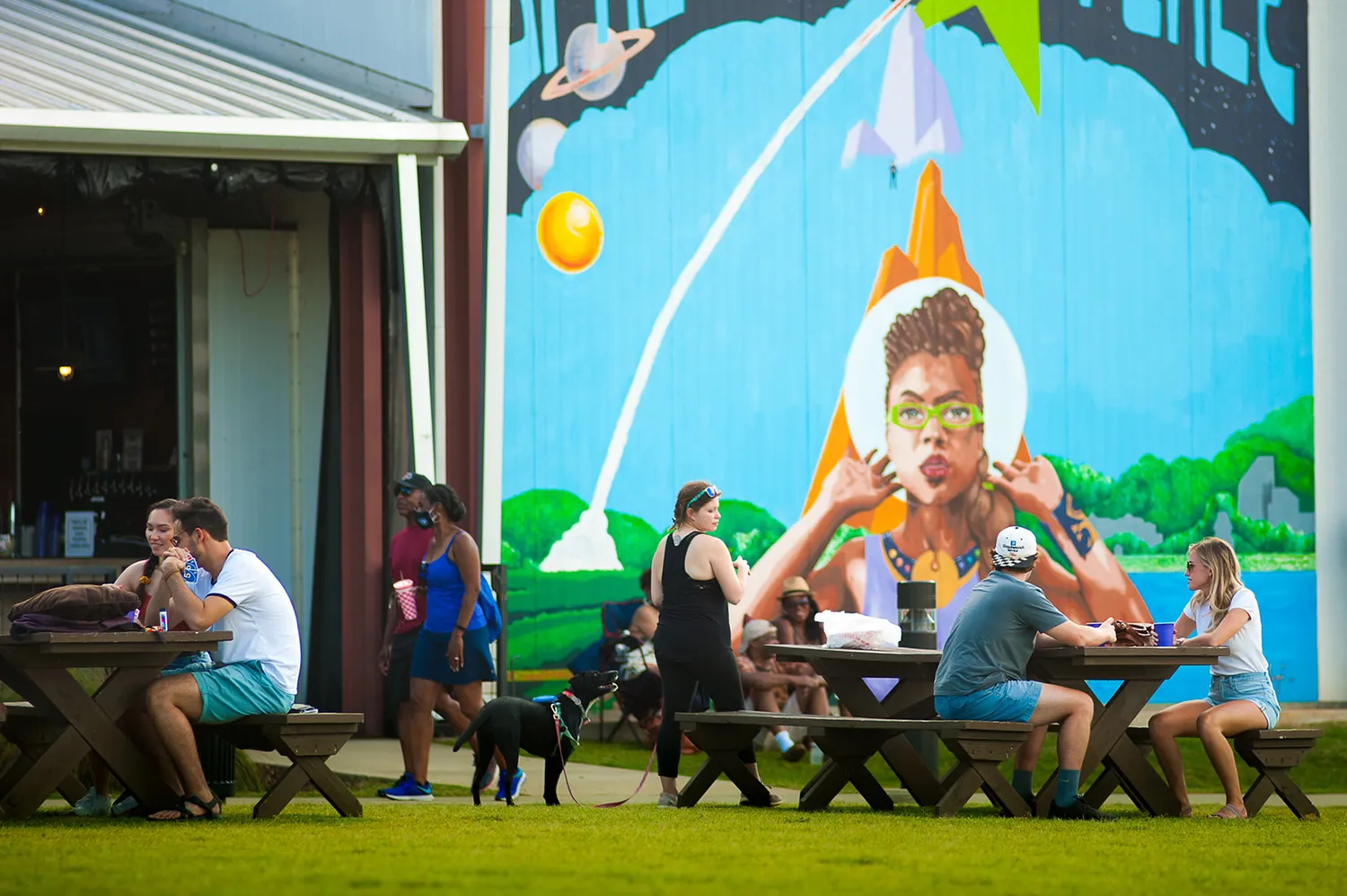 People enjoying food and drinks at outdoor tables near the vibrant mural art at Campus 805.