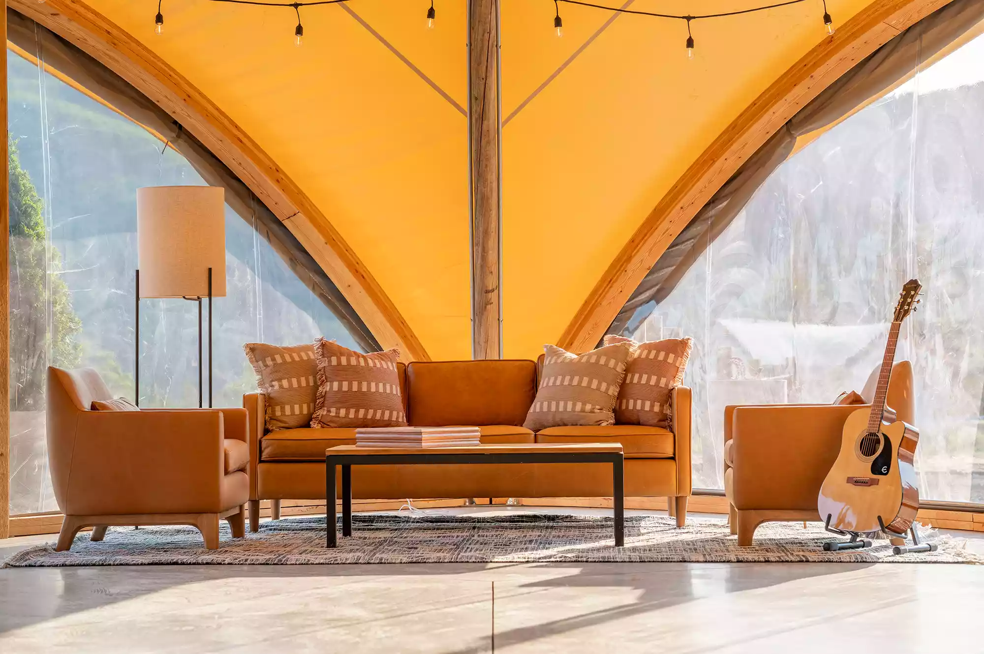 A cozy lounge area inside a large canvas tent with mid-century modern sofas and chairs for communal gathering.