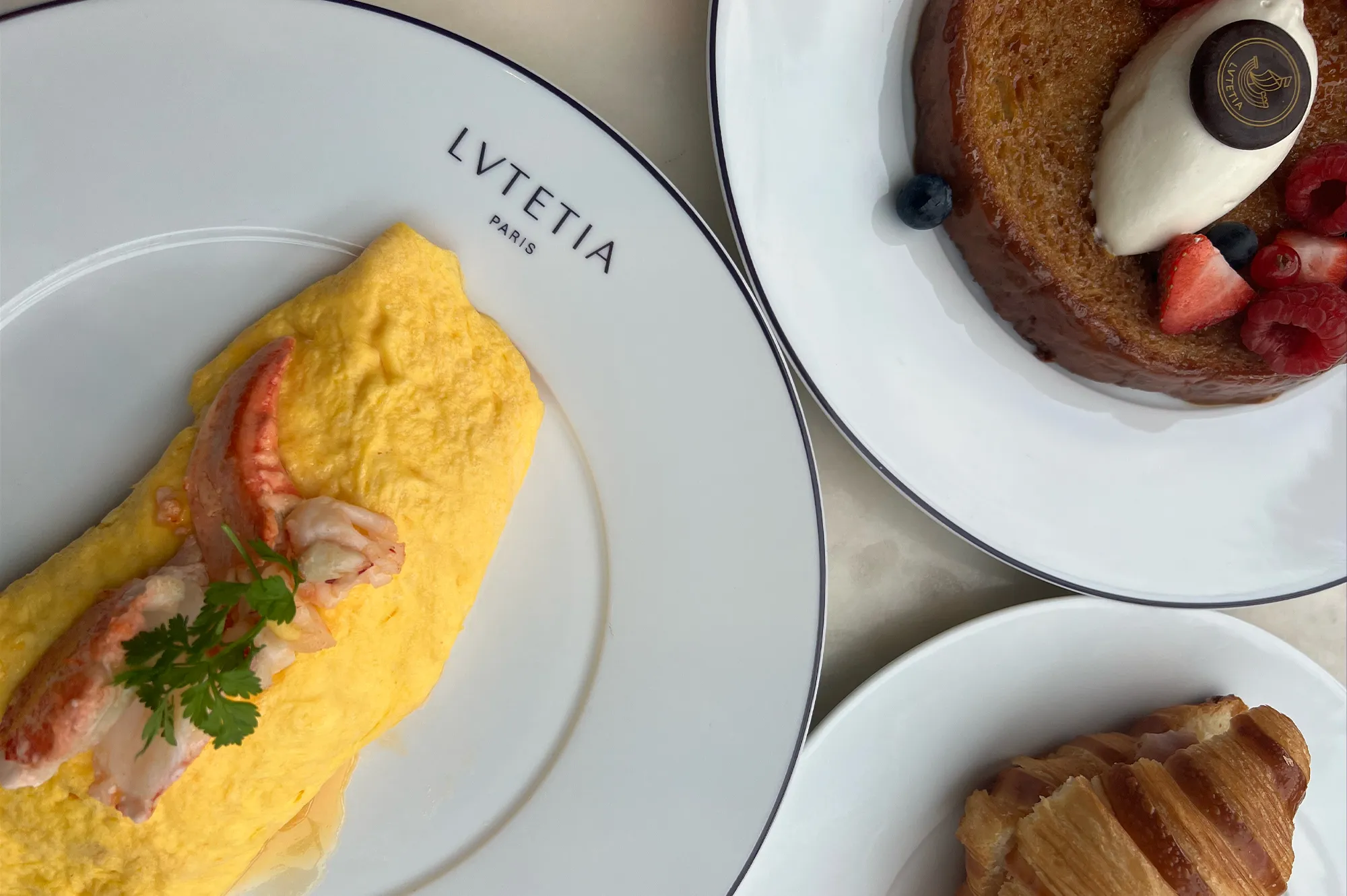 Plates of gourmet breakfast items including a lobster omelette and fresh pastries on a white tablecloth.