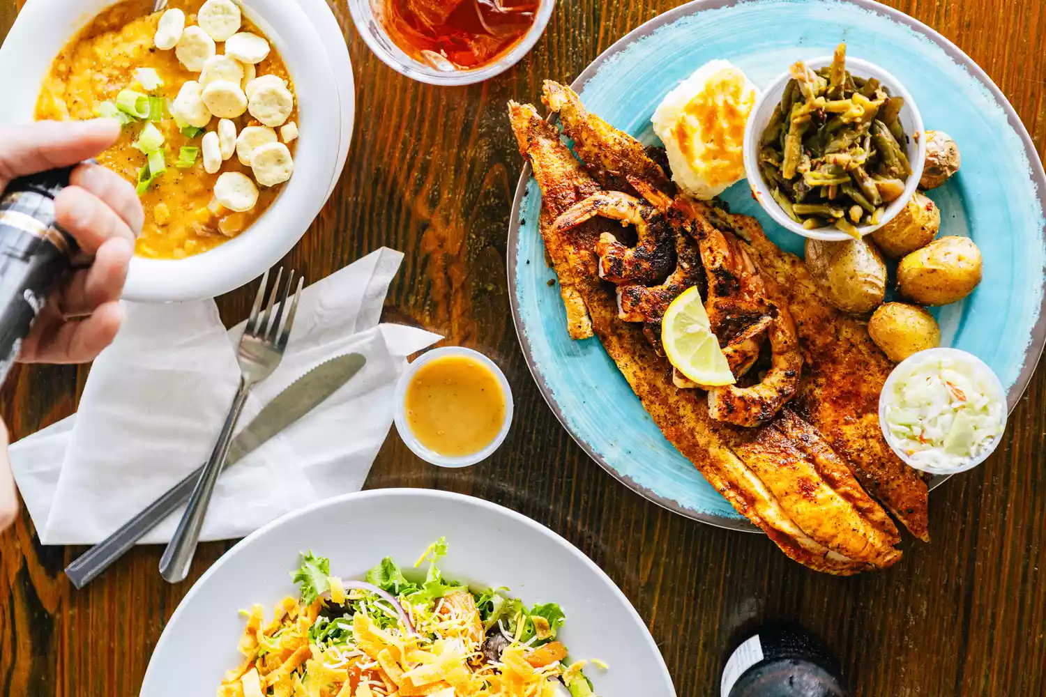 A restaurant table spread featuring grilled fish, shrimp and corn chowder, and fresh salads.