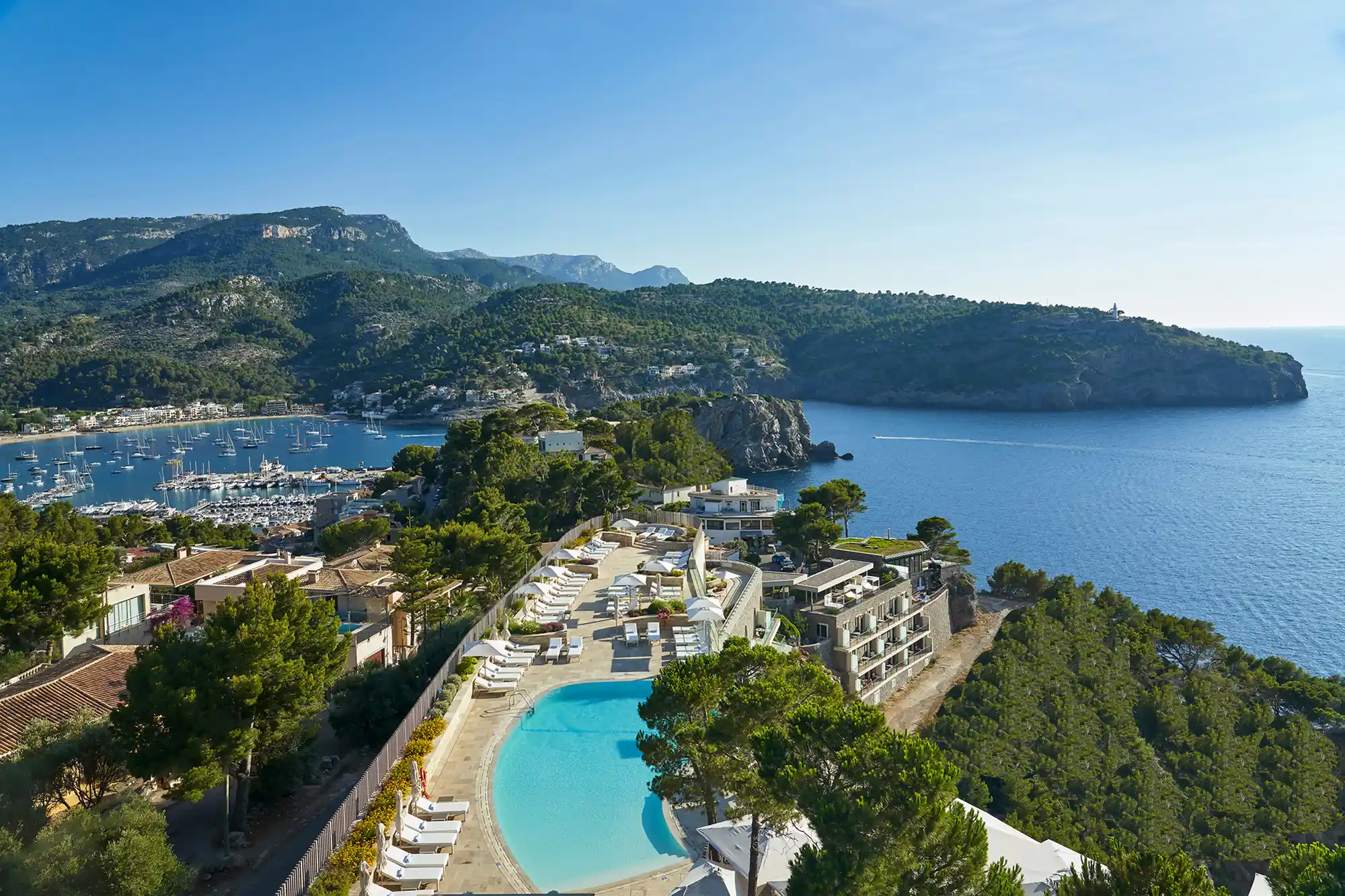 A luxury coastal resort pool area with views of the bay and Mediterranean trees.