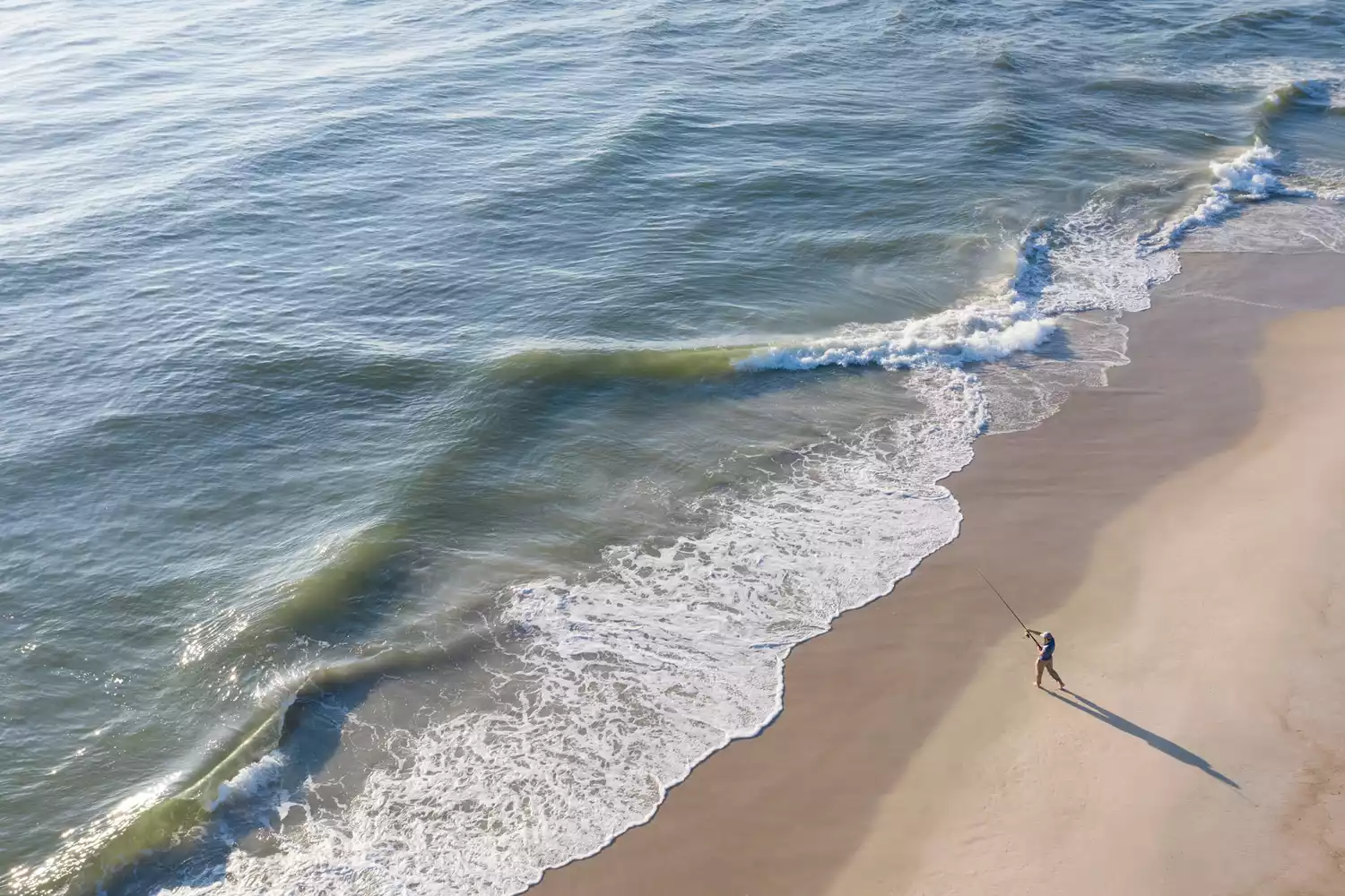 A fisherman standing on the shoreline of the Atlantic Ocean at daytime.