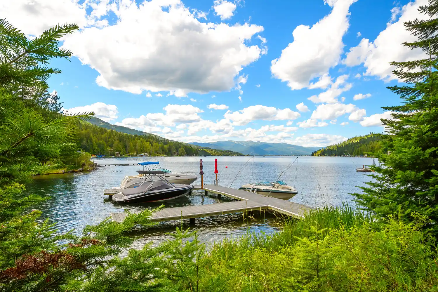 A wooden dock with several motorboats moored on the expansive Lake Pend Oreille with mountains in the background.