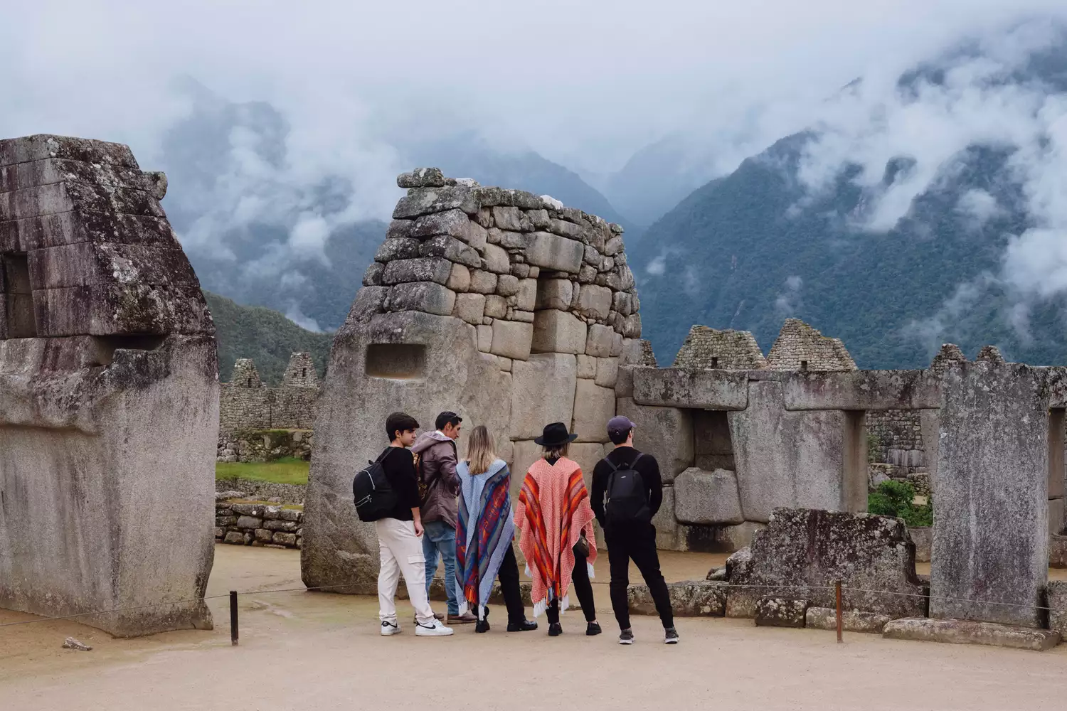 A group of tourists exploring the stone ruins of Machu Picchu with mountains in the background.