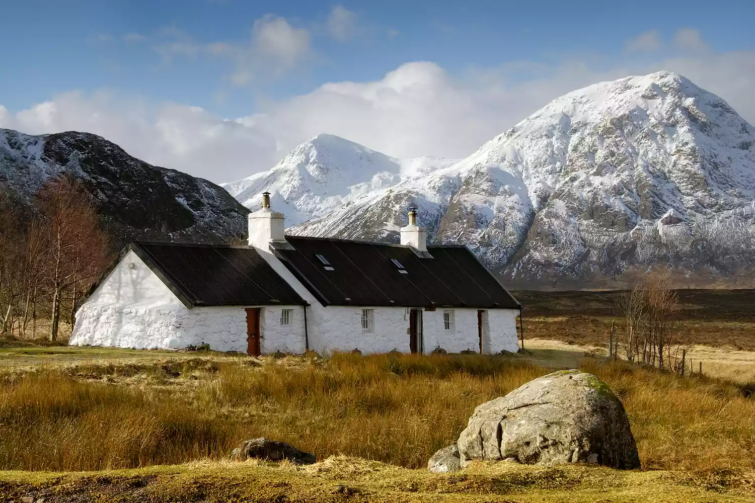 The small white Black Rock Cottage in Glencoe surrounded by snow-dusted mountains.