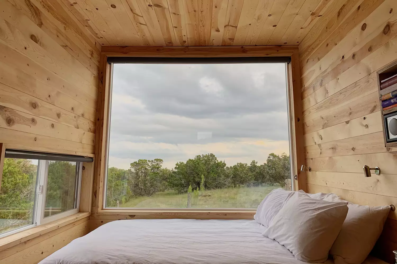 Interior view of a modern tiny home with a large picture window looking out onto a forest.