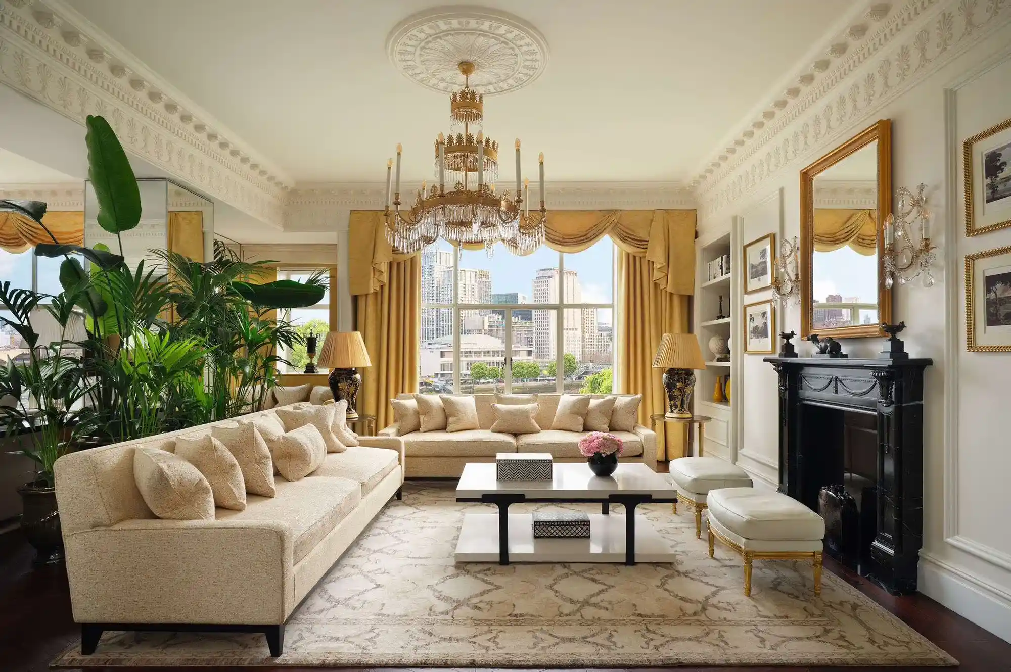 A luxury hotel living room with elegant furniture, a chandelier, and a large window overlooking a city.