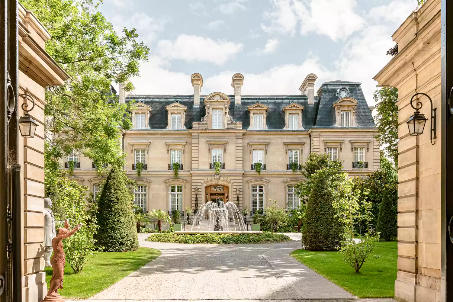 The stately stone facade of the Saint James Paris hotel surrounded by greenery.