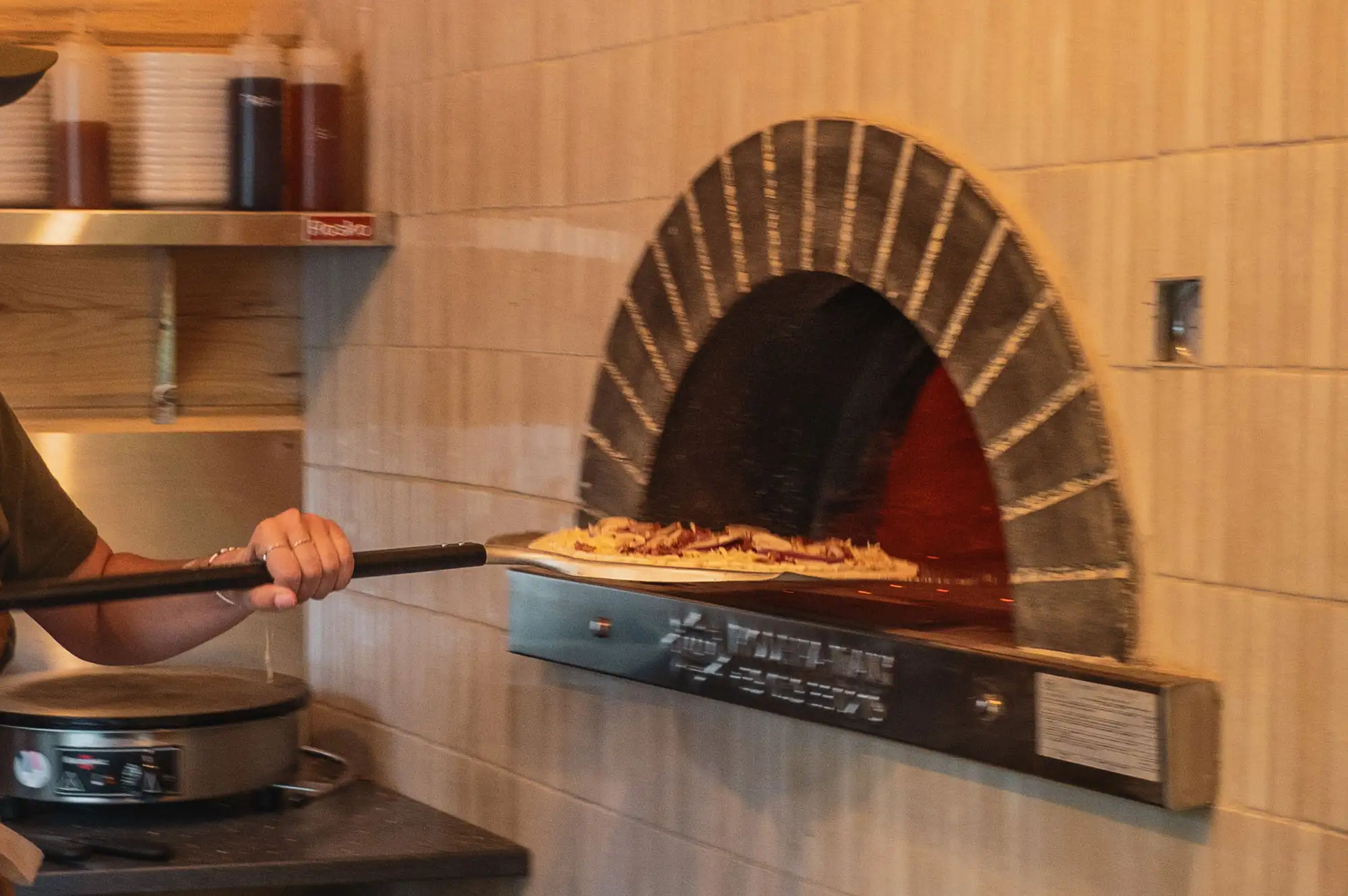 A chef using a traditional pizza peel to bake a pizza in a large commercial brick oven.