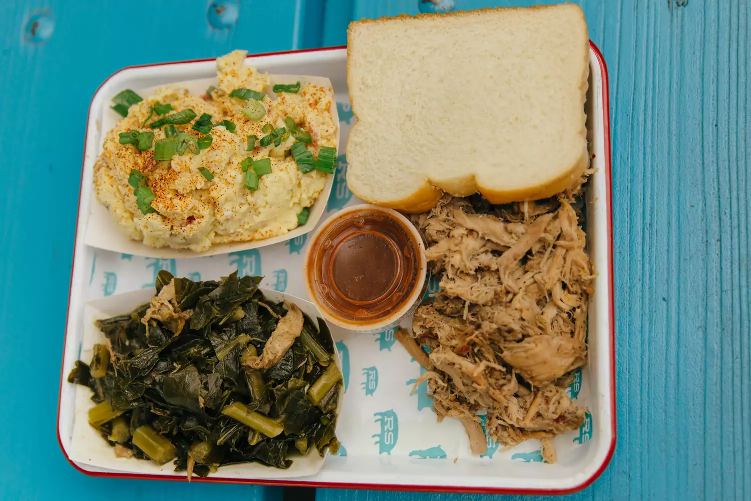 A tray of authentic Southern pulled pork BBQ with mac and cheese and collard greens.