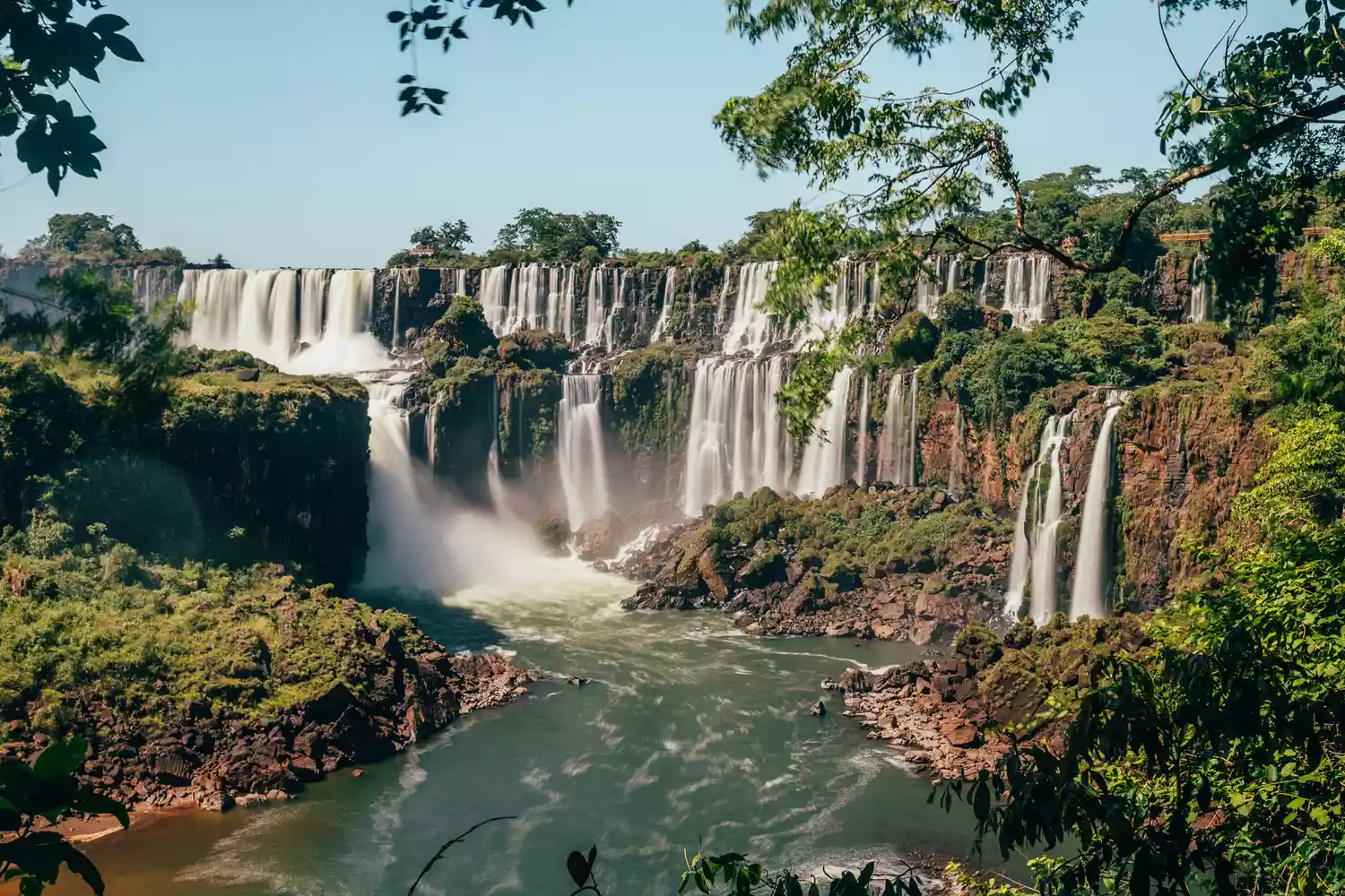 Panoramic view of the massive Iguazu Falls with water cascading over lush green cliffs.