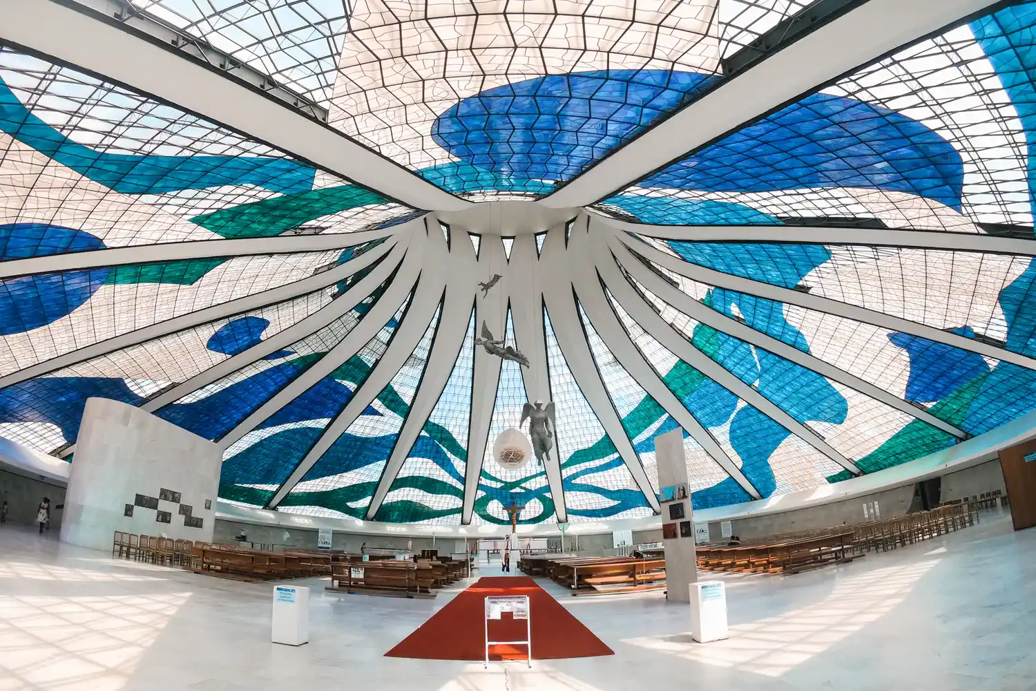 The interior of the Cathedral of Brasília featuring blue and white stained glass and hanging angel sculptures.