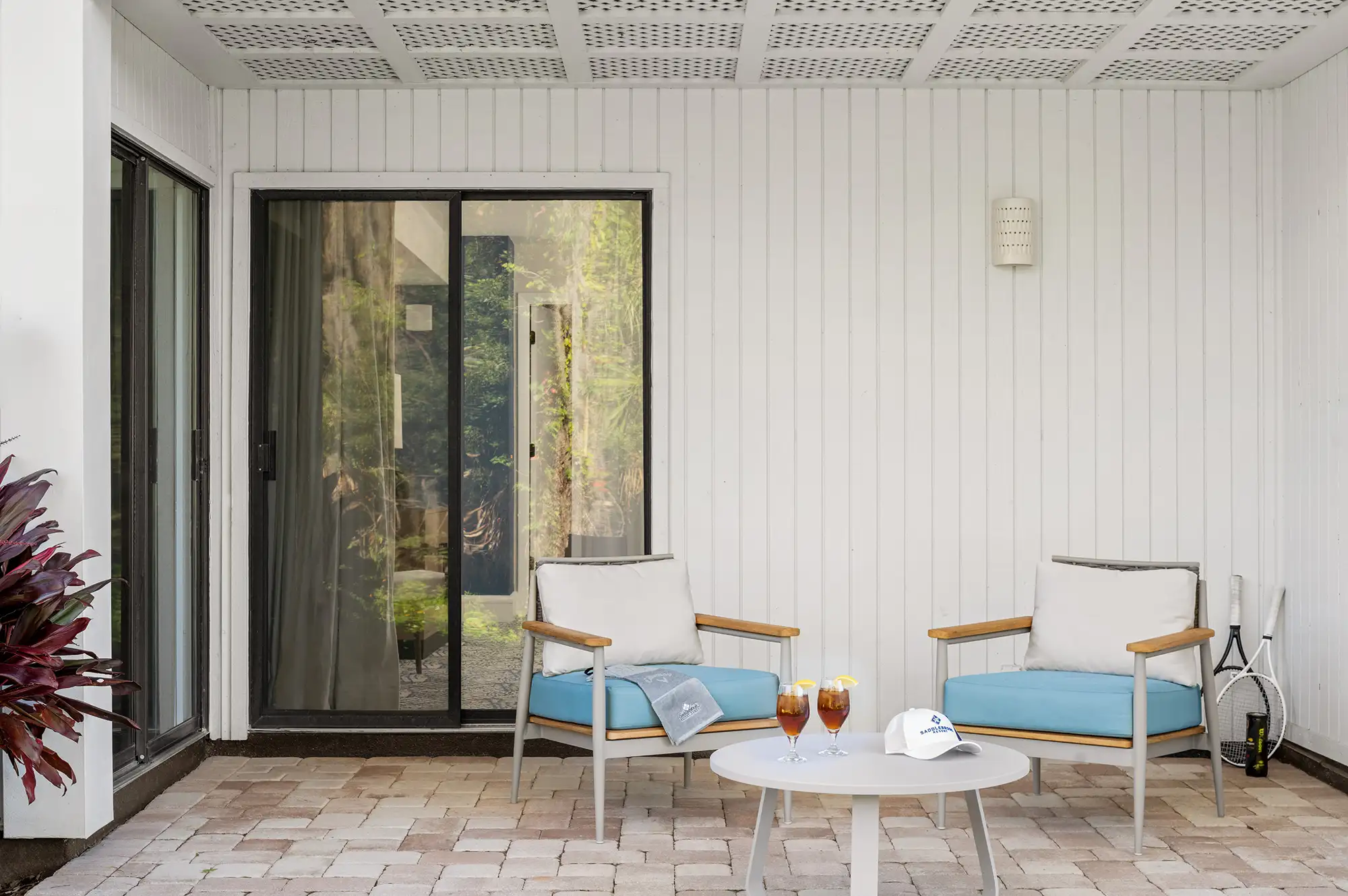 A resort patio featuring tennis rackets, drinks, and outdoor seating visible through a glass door.