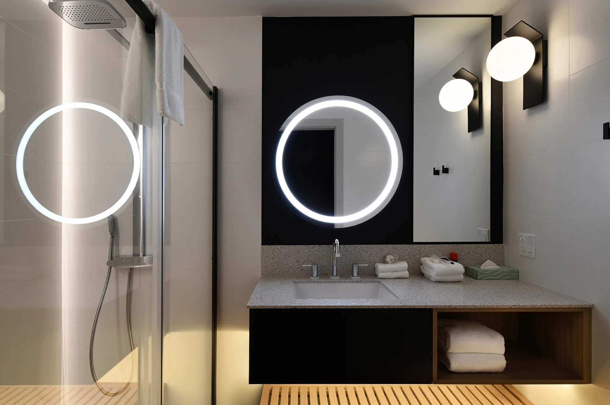 A sleek modern bathroom with a large backlit mirror and minimalist tiling.