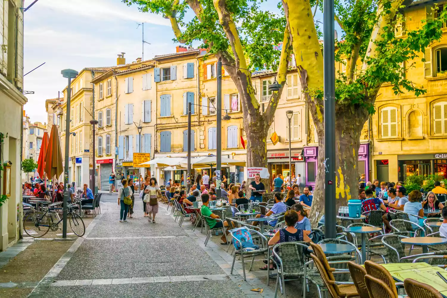 Pedestrians walking along a narrow, picturesque stone street in the center of Avignon.